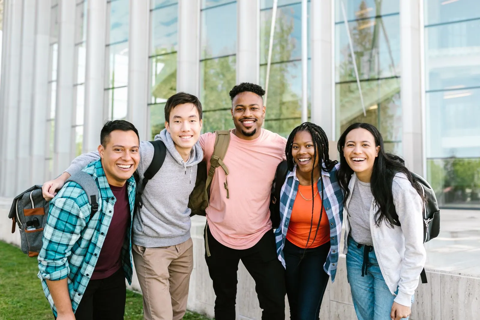 Groupe d'étudiants souriants, bras sur les épaules, devant un bâtiment universitaire